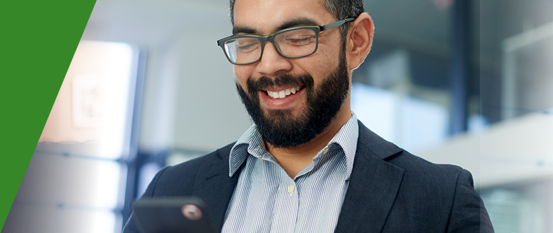 A person in a business suit is holding a phone and smiling while looking at it.